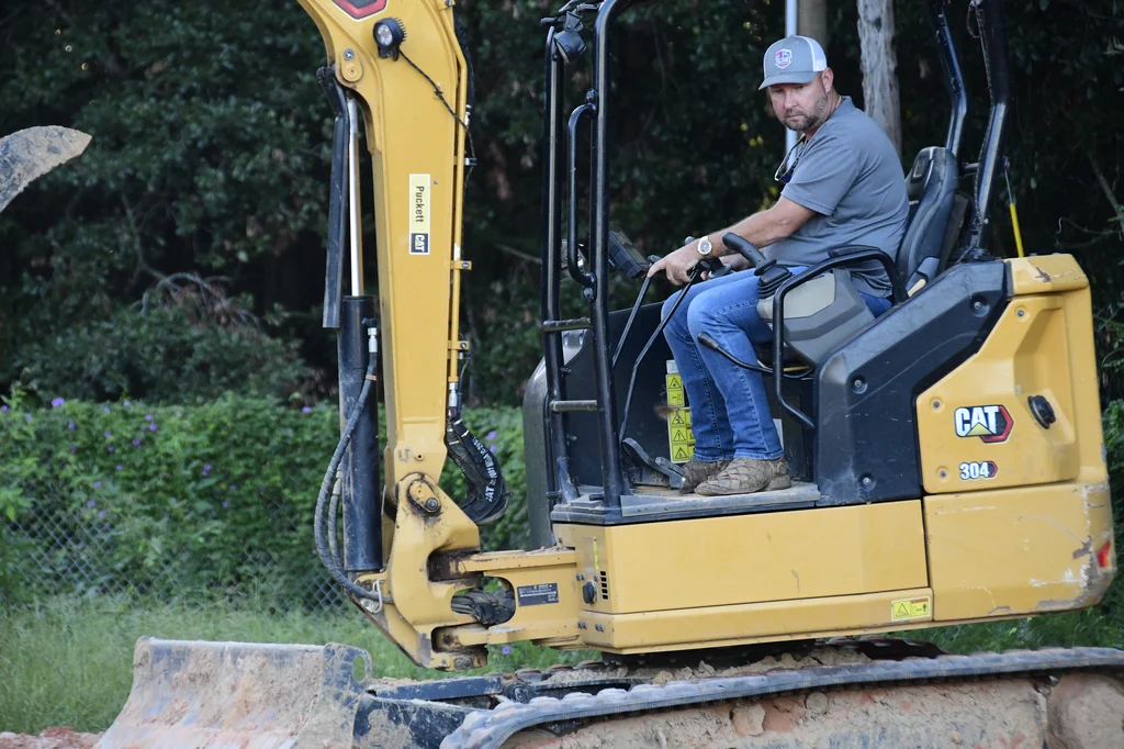 Reliance crew member seated at the controls of a compact excavator.